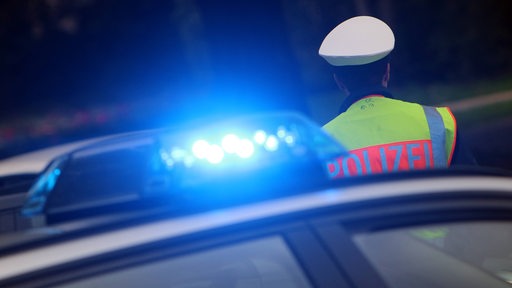Ein Polizist steht hinter einem Polizeiauto mit eingeschalteter Blaulichtanlage