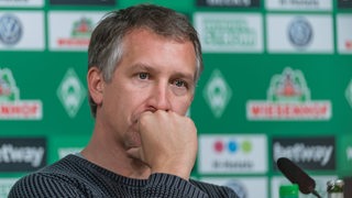 Baumann schaut nachdenklich mit der Hand am Mund während einer Pressekonferenz.