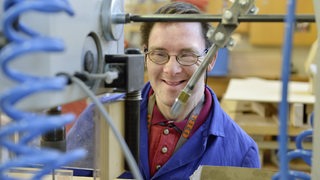 Ein Mann mit dem Down Syndrom arbeitet in einer Werktstatt an einer Maschine.