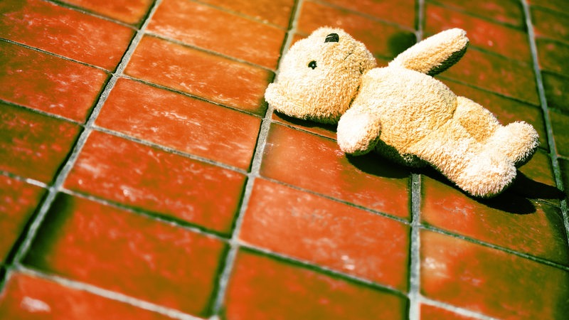 Ein Teddy liegt auf kaltem Fliesenboden.