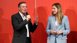 Das Foto zeigt einen Mann, Frank Imhoff, und eine Frau, Wiebke Winter, vor rotem Hintergrund.