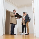 Ein Makler zeigt einem jungen Mann und einer älteren Frau eine leerstehende Wohnung