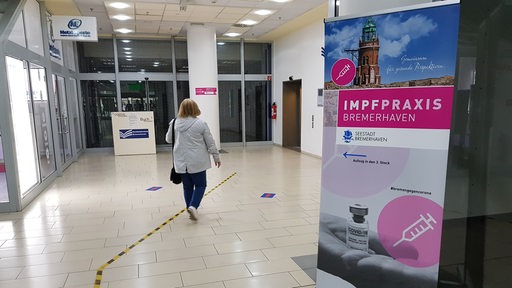 Eine Frau läuft an einem Schild mit der Aufschrift "Impfpraxis Bremerhaven" vorbei.