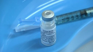 Der Impfstoff der Firma Novavax, im Hintergrund eine Impfspritze. 