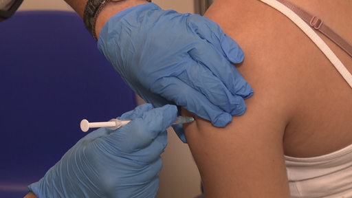 Eine Person mit blauen Handschuhen setzt einer Patientin eine Spritze mit Impfstoff.