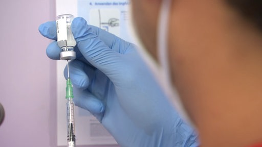 Eine Person mit blauen Handschuhen bereitet eine Impfung mit einer Spritze vor.
