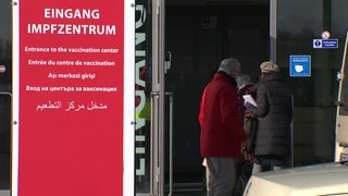 Der Eingang vom Impfzentrum in Bremen mit einem großen roten Schild davor. Drei ältere Menschen gehen gerade hinein.