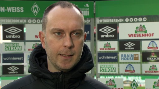 Werder-Trainer Ole Werner beim Interview nach dem Spiel vor einer Werbewand.