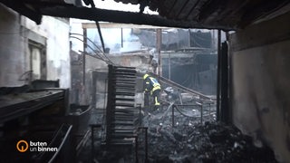Ein ausgebranntes Gebäude, ein Feuerwehrmann steht darin.