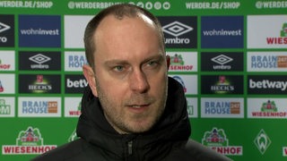Werder-Trainer Ole Werner nach dem Spiel vor einer Werbewand im Interview.