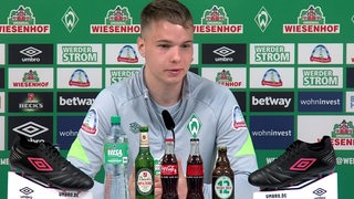 Werder-Profi Niklas Schmidt sitzt vor einer Werbewand beim Interview.