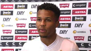 Werder-Spieler Felix Agu steht vor einer Werbewand bei einem Interview.