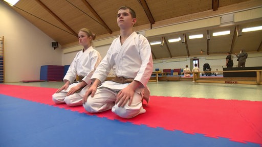 Die Karate-Talente Rani Wienbeck und Asim Malsagov knien neben der Kampfmatte.