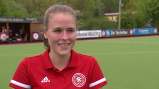 Hockey-Spielerin Lena Frerichs lächelt während eines Interviews auf dem Spielfeld.