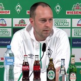 Werder-Coach Ole Werner im weißen Kapuzenshirt vor einer Werbewand beim Interview.
