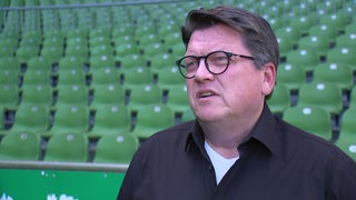 Werder-Präsident Hubertus Hess-Grunewald gibt im Innenraum des Weser-Stadions vor den grünen Sitzreihen ein Interview.