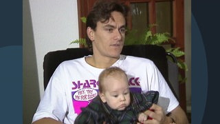 Werder-Spieler Wynton Rufer gibt ein Interview, während sein Kind auf seinem Schoß sitzt.