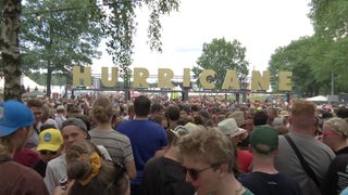 Viele Menschen stehen auf einem Festival. Etwas über ihnen ist er Schriftzug "Hurricane" zu sehen.