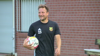 Heeslingen-Spieler Philipp Bargfrede geht nach dem Training lächelnd mit einem Ball im Arm vom Platz.