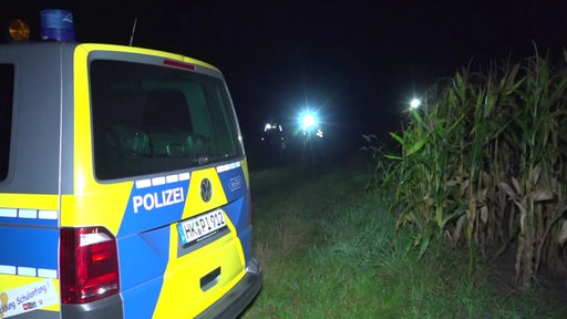 Ein Polizeiwagen auf einem Feld, im Hintergrund Taschenlampen.