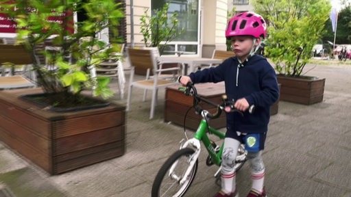 Der 4-jährige Kalle schiebt sein Fahrrad den Gehweg entlang