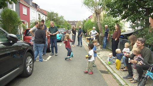 In der Nachbarschaft stehen verschiedene Menschen von jung bis alt zusammen, spielen und tauschen sich aus. 