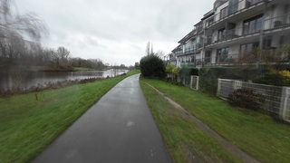 Das Foto zeigt einen Weg, auf der linken Seite die kleine Weser, auf der rechten Wohnhäuser.