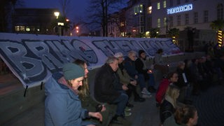 Demonstranten sitzen vor dem Bremer Theater bei Nacht