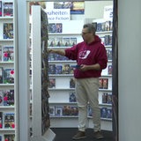 Ein Mann steht zwischen Regalen voller DVDs und ordnet Filme weg.