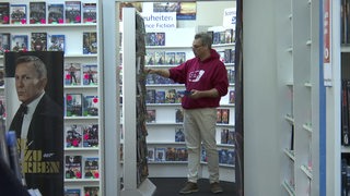 Ein Mann steht zwischen Regalen voller DVDs und ordnet Filme weg.