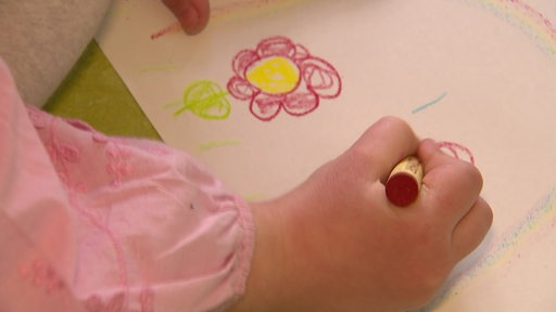 Eine Kinderhand malt eine bunte Blume auf ein Papier