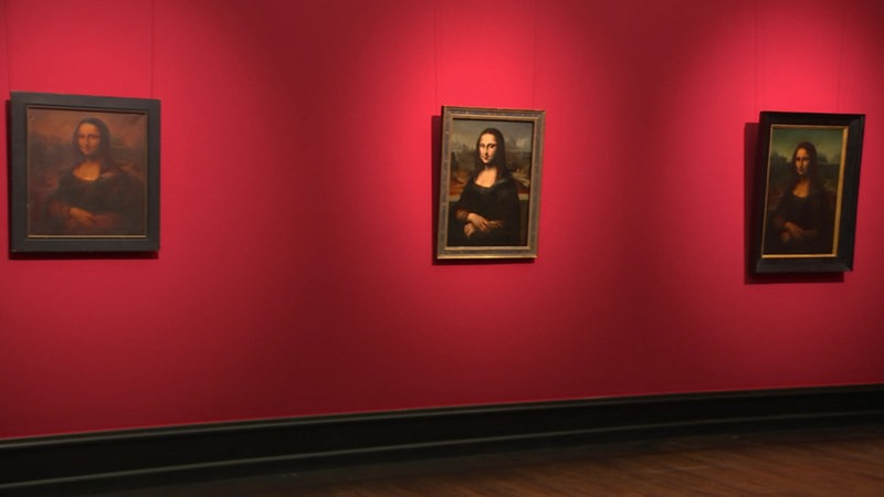 Mehrere Mona-Lisa Kopiel hängen an einer roten Wand. 
