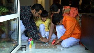 Eine Familie malt ein traditionelles indisches Bild auf dem Boden.
