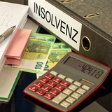 Ein Taschenrechner liegt auf Hundert-Euro-Scheinen und vor einem Aktenordner mit der Aufschrift "Insolvenz".