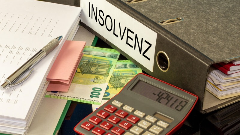 Ein Taschenrechner liegt auf Hundert-Euro-Scheinen und vor einem Aktenordner mit der Aufschrift "Insolvenz".