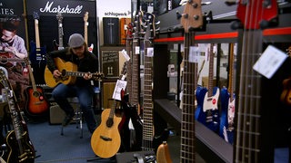 Ein Mann sitzt in einem Geschäft für Musikinstrumente auf einem Hocker und spielt Gitarre.
