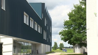 Ein wellblechartiges Gebäude mit kräftigen Blauton, die Kunsthochschule von draußen. 