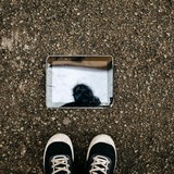 Ein kaputtes Tablet liegt auf dem Boden, davor zwei Füße. 