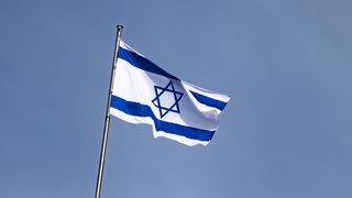 Vor blauem Himmel weht eine blau-weiße Flagge mit Stern an einem Fahnenmast.