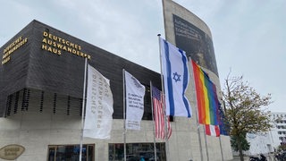 Vor einem einem Gebäude wehen mehrere Flaggen, darunter die blau-weiße von Israel.