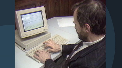 Ein Mann sitzt vor einem alten Computer mit kastenförmigen Bildschirm.