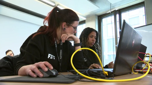 Zwei Frauen sitzen hinter Computern und schauen konzentriert auf den Bildschirm.