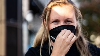 Eine junge Frau, die Maske tragend in die Kamera schaut