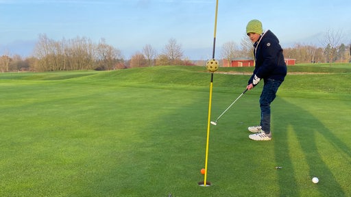 Ein Junge, der mit einem Schläger einen Golfball trifft