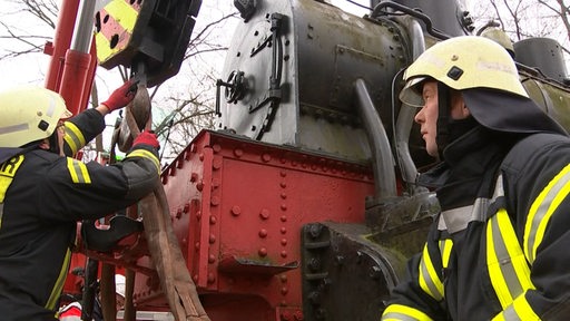 Zwei Feuerwehrmänner arbeiten an einer Lok in Bremen