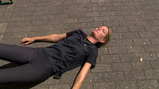 Reporterin Janna Betten liegt in einer Pause vom 50 km "Megamarsch" auf dem Boden und ruht sich aus.
