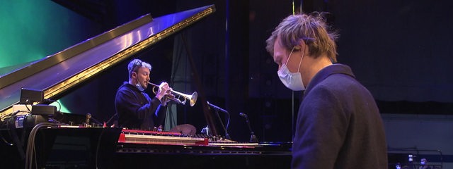 Ein Pianist und ein Trompeter spielen zusammen Musik auf einer Bühne.