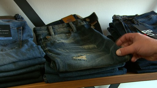 Unterschiedliche Jeans- Hosenmodelle liegen in einem Regal.