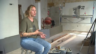 Junge Frau sitzt in einer Baustelle eines Hauses und erzählt