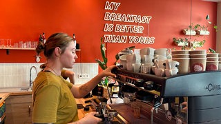 Eine junge Frau macht in einem Cafe Kaffee.